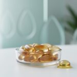 Close-up of CBD gel capsules in a glass dish on a clean surface, photographed in soft natural light with a blurred green plant background.